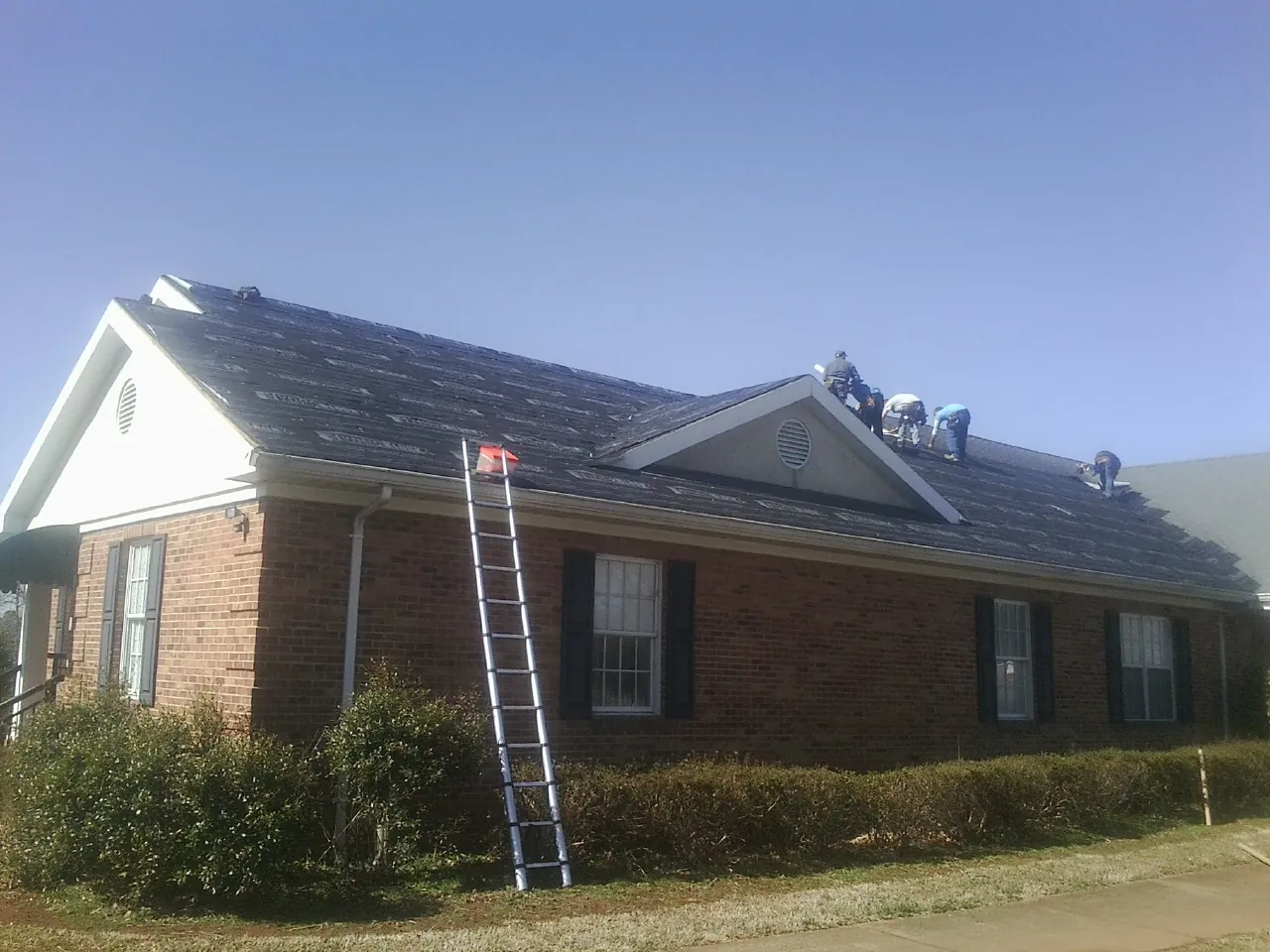 Crew tearing shingles off a brick ranch roof with a ladder set — Metal Roof Repair work by our crew in Mason